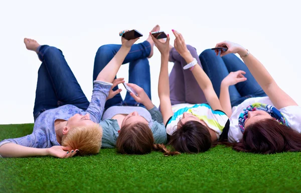 Vier jonge vrouwen liggen op groen gras met mobiele telefoon — Stockfoto