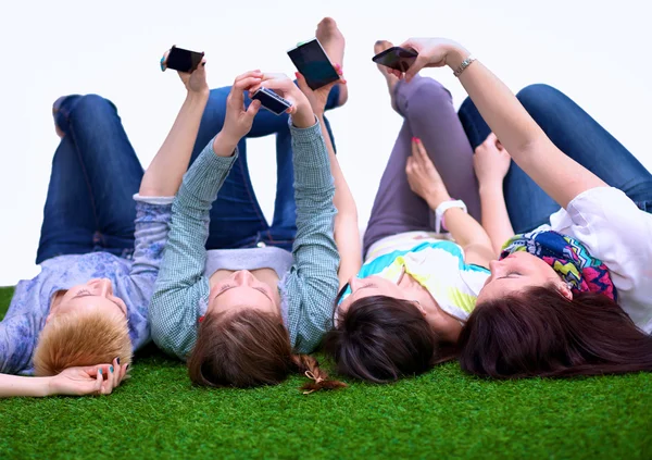 Cuatro mujeres jóvenes tumbadas en hierba verde con teléfono móvil — Foto de Stock