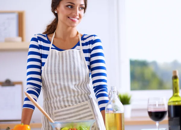 Hymyilevä nuori nainen sekoittamalla tuoretta salaattia, seisoo lähellä pöytää — kuvapankkivalokuva