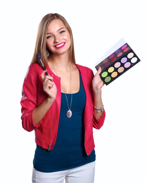 Joven hermosa mujer sostiene en una mano y una paleta con pintura y sombras para el maquillaje, cepillo de segunda mano para maquillaje —  Fotos de Stock