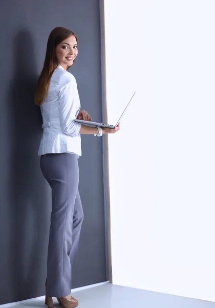 Jonge vrouw met een laptop, staande op een grijze achtergrond — Stockfoto