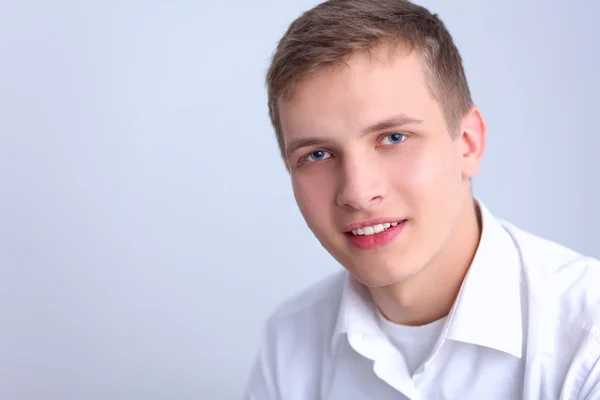 Portret van een jonge man die lacht zittend op grijze achtergrond — Stockfoto