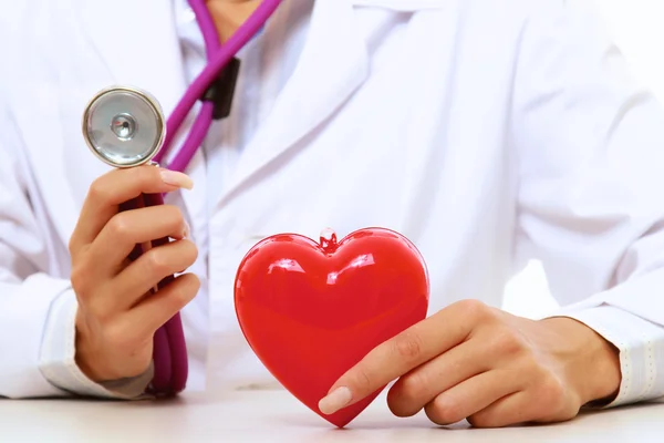 Une femme médecin souriante examinant un cœur rouge — Photo