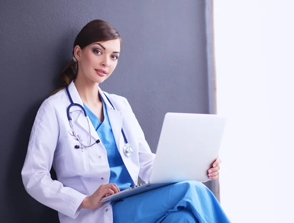 Женщина-врач, сидящая на сером фоне — стоковое фото