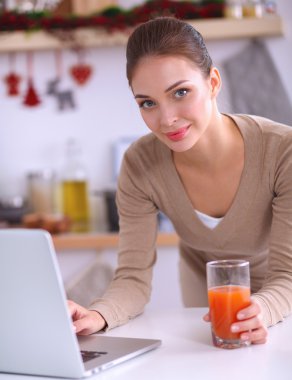 mutfağında suyu yudumlarken bir dizüstü bilgisayar kullanan kadın