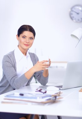 Genç bir iş kadını ofisinde fincanla masada oturuyor.