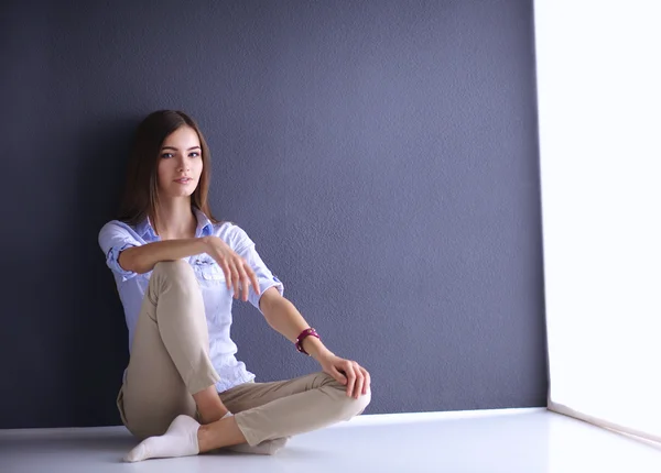 Portrait of young woman sitting on the floor near dark wall — Stock Photo, Image