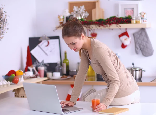 Woman using a laptop while drinking juice in her kitchen — Stock Photo, Image