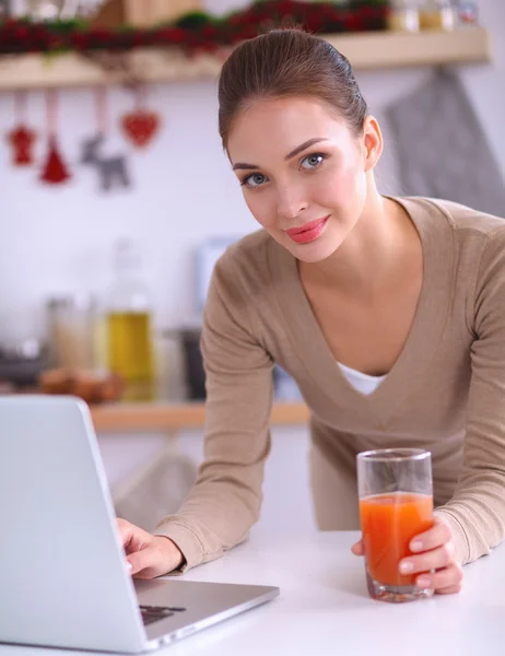 Femme utilisant un ordinateur portable tout en buvant du jus dans sa cuisine — Photo