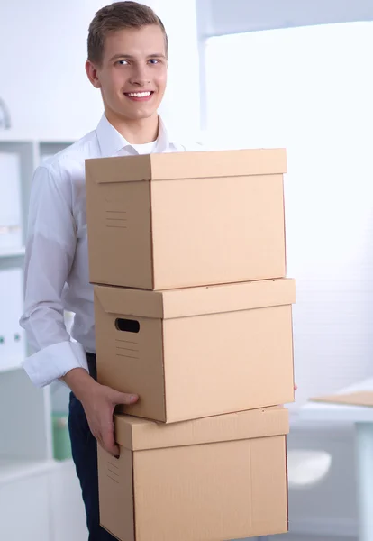 Young Man holding a stack of cardboard boxes standing in office — Stock Photo, Image