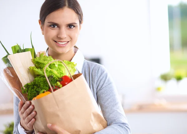 Jovem segurando supermercado saco de compras com legumes de pé na cozinha. — Fotografia de Stock