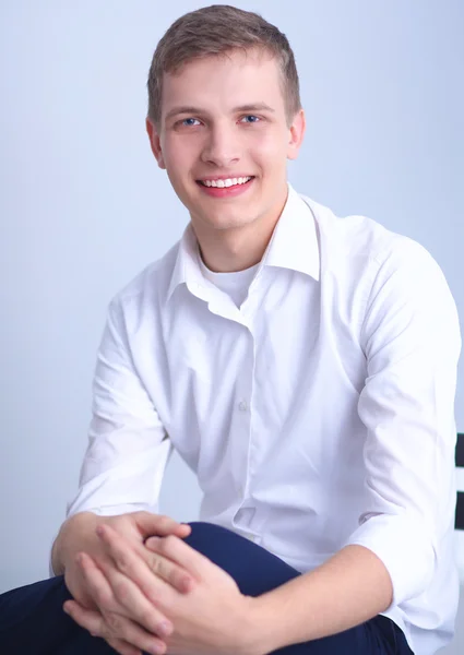 Retrato de jovem sorrindo sentado em fundo cinza — Fotografia de Stock