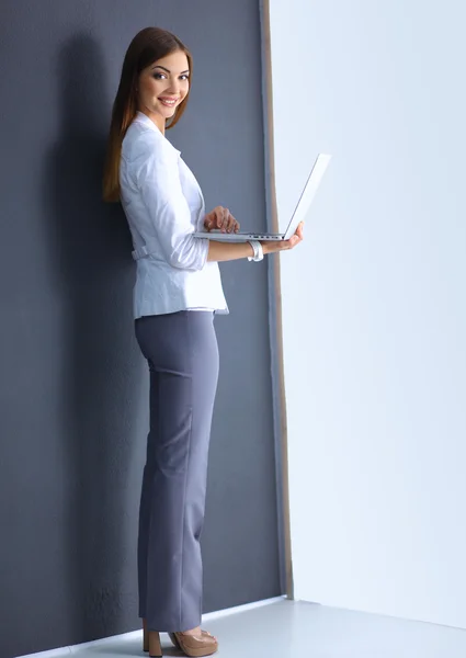 Jonge vrouw met een laptop, staande op een grijze achtergrond — Stockfoto