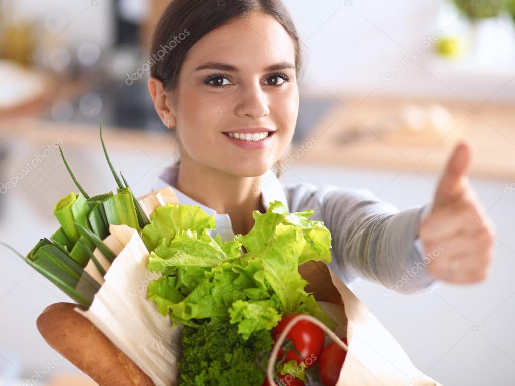 Young woman holding grocery shopping bag with vegetables and showing ok