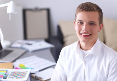 Genç işadamı ofiste çalışıyor, masada oturuyor.