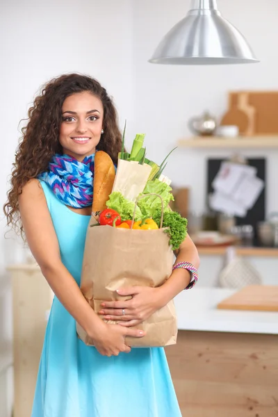 Giovane donna che tiene la spesa con verdure In piedi in cucina. — Foto Stock