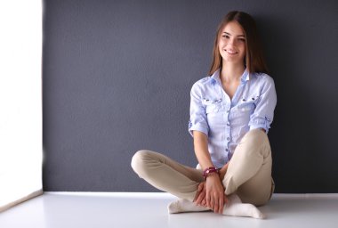 Genç bir kadın yerde, kara duvarın yanında oturuyor.