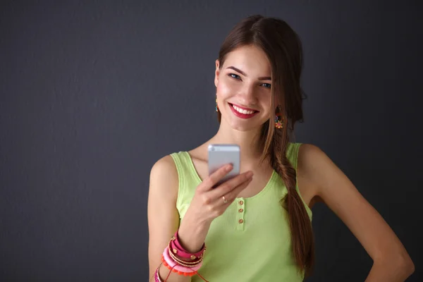 Krásná mladá žena drží mobil, stojící poblíž tmavé stěny — Stock fotografie