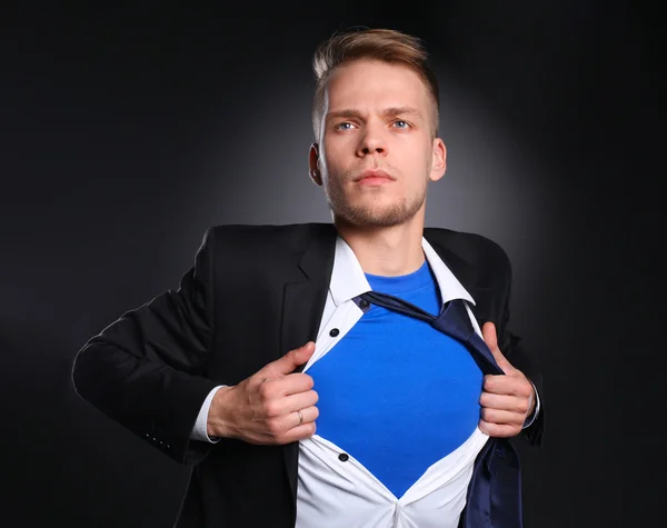 Jonge zakenman handelt zoals een super held en scheuren zijn overhemd, geïsoleerd op grijze achtergrond — Stockfoto