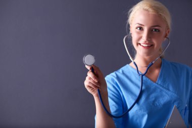 Steteskopla dinleyen kadın doktor, gri arka planda izole edilmiş.