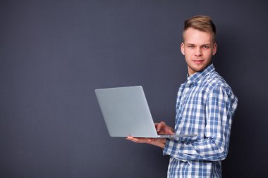 Gri arka plan üzerinde dizüstü bilgisayar konumu olan kendine güvenen genç adam portresi