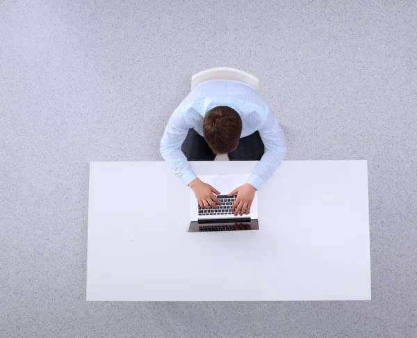 Молодой человек работает на ноутбуке, сидит за столом в офисе — стоковое фото