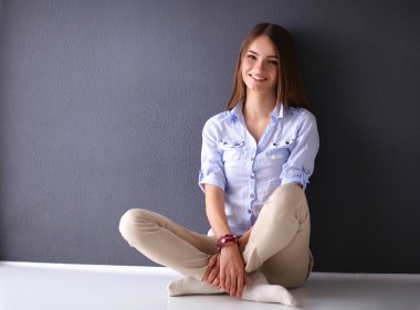 Genç bir kadın yerde, kara duvarın yanında oturuyor.