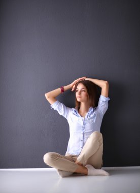 Genç bir kadın yerde, kara duvarın yanında oturuyor.