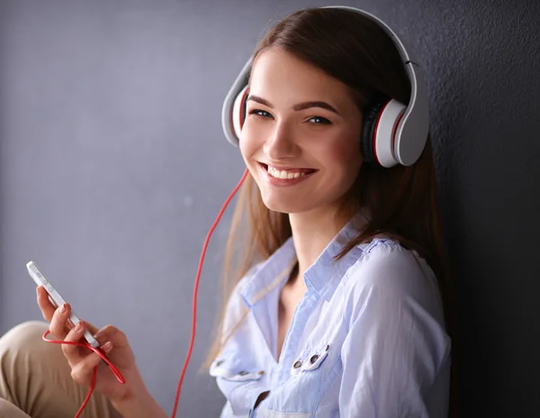Усміхнена дівчина з навушниками сидить на підлозі біля стіни — стокове фото