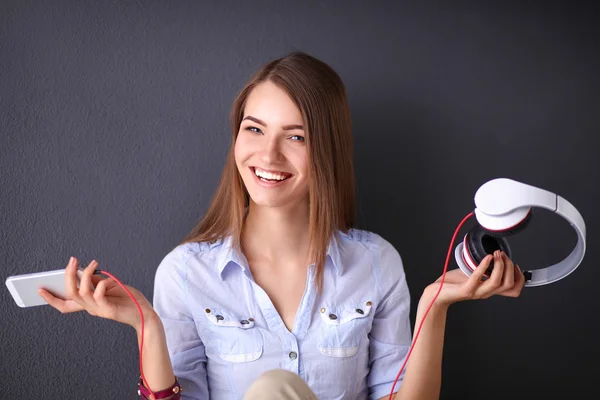 Chica sonriente con auriculares sentados en el suelo cerca de la pared —  Fotos de Stock