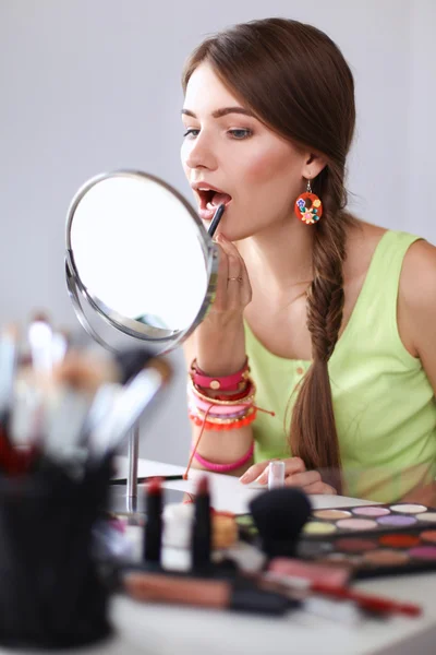 Jeune belle femme se maquillant près du miroir, assise au bureau — Photo