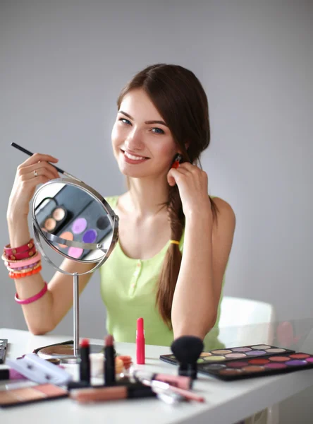 Joven hermosa mujer haciendo maquillaje cerca del espejo, sentado en el escritorio — Foto de Stock