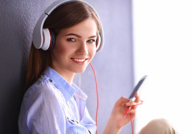 Duvara yakın katta oturan kulaklıklar ile gülümseyen kız