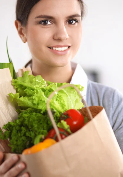 야채가 담긴 식품권을 든 젊은 여자 가 부엌에 서 있다 — 스톡 사진