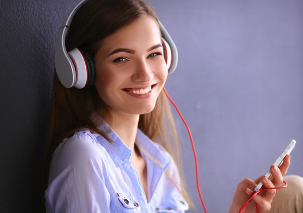 Usměvavá dívka s sluchátka sedí na podlaze u zdi — Stock fotografie