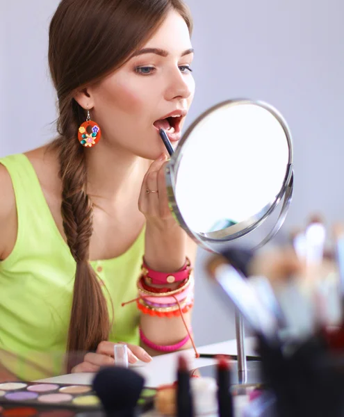 Joven hermosa mujer haciendo maquillaje cerca del espejo, sentado en el escritorio —  Fotos de Stock
