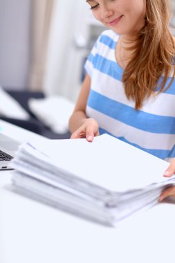 Elinde evrakları olan kadın masanın üstünde oturuyor.