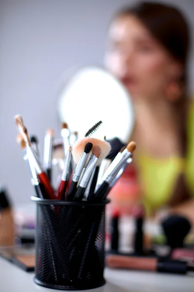 Joven hermosa mujer haciendo maquillaje cerca del espejo, sentado en el escritorio —  Fotos de Stock