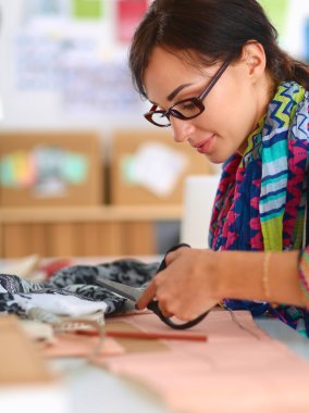 Moda tasarımcısı dikiş makinesinin yanında tekstil kesiyor.