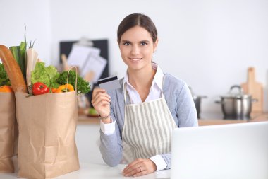 Mutfakta bilgisayar ve kredi kartı kullanan gülümseyen bir kadın.
