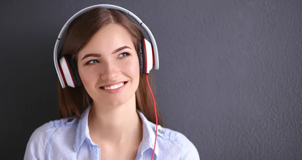 Menina sorridente com fones de ouvido sentado no chão perto da parede — Fotografia de Stock