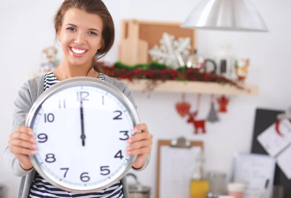 Glückliche junge Frau zeigt Uhr in weihnachtlich dekorierter Küche — Stockfoto