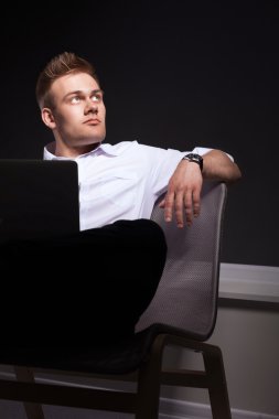 Gri arka plan üzerinde dizüstü bilgisayar konumu olan kendine güvenen genç adam portresi