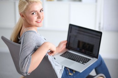 Genç ve güzel bir kadın evde dizüstü bilgisayar kullanıyor.