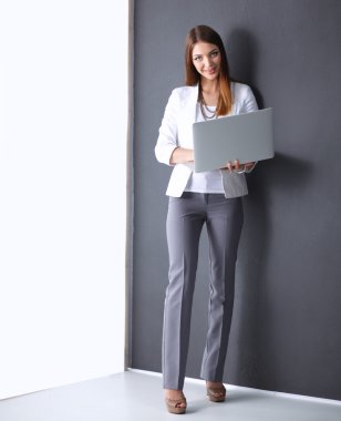 Bir dizüstü bilgisayar, gri arka plan üzerinde ayakta tutan genç kadın