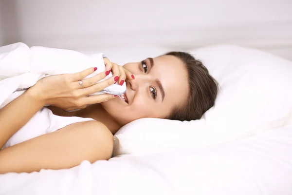 A pretty young woman peeking from under the covers in her bedroom happilly — Stock Photo, Image