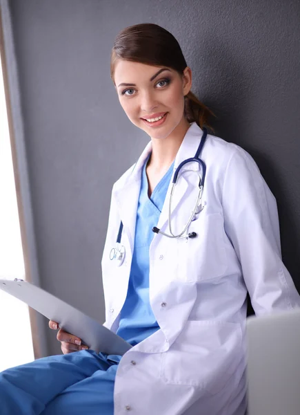 Médico femenino trabajando sentado sobre fondo gris Imagen de stock