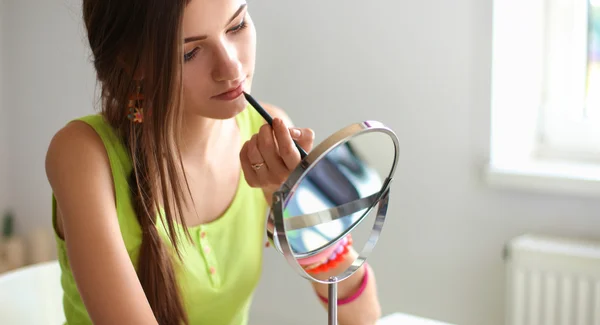 Joven hermosa mujer haciendo maquillaje cerca del espejo, sentado en el escritorio — Foto de Stock