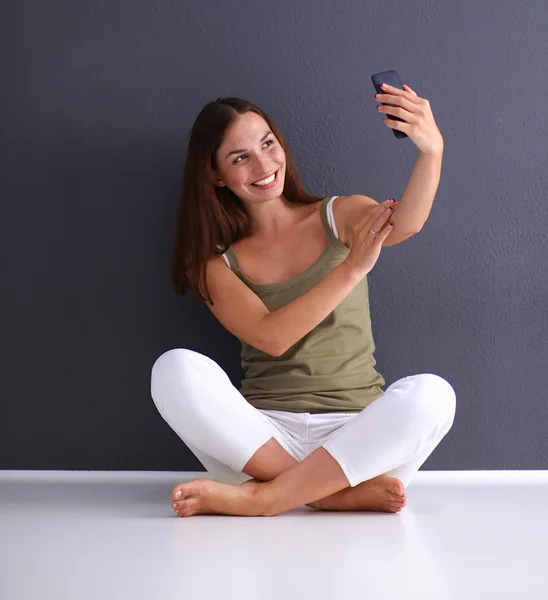 Atractiva chica caucásica sentada en el suelo sosteniendo móvil — Foto de Stock
