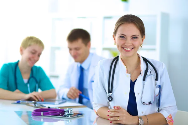 Hermosa joven sonriente doctora sentada en el escritorio —  Fotos de Stock